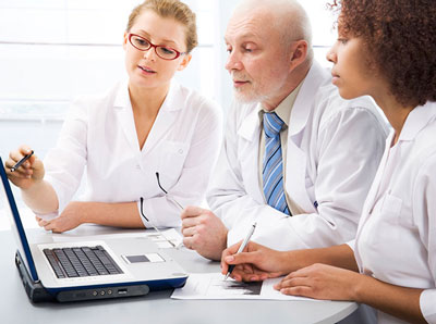 Three people in lab coats looking at a computer 