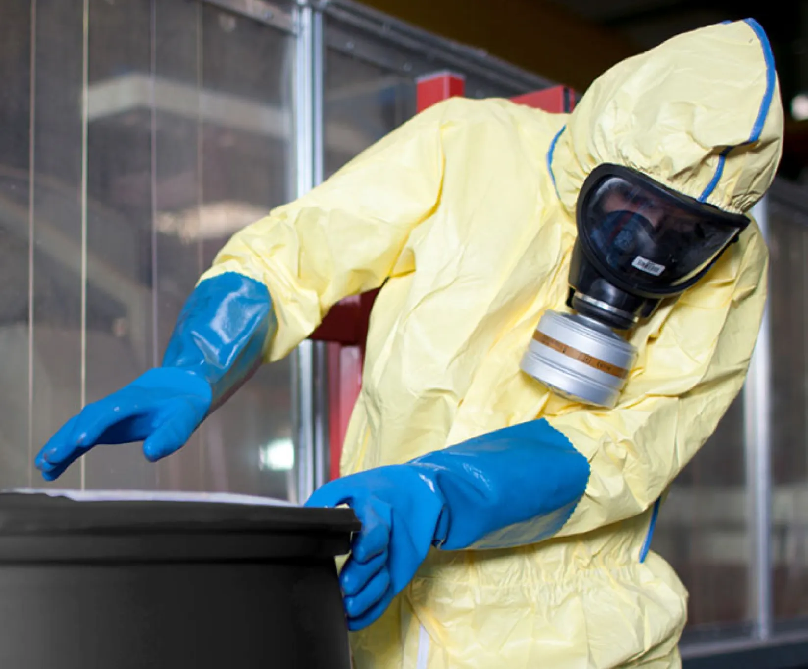 A person in a hazmat suit handling material in a black barrel.