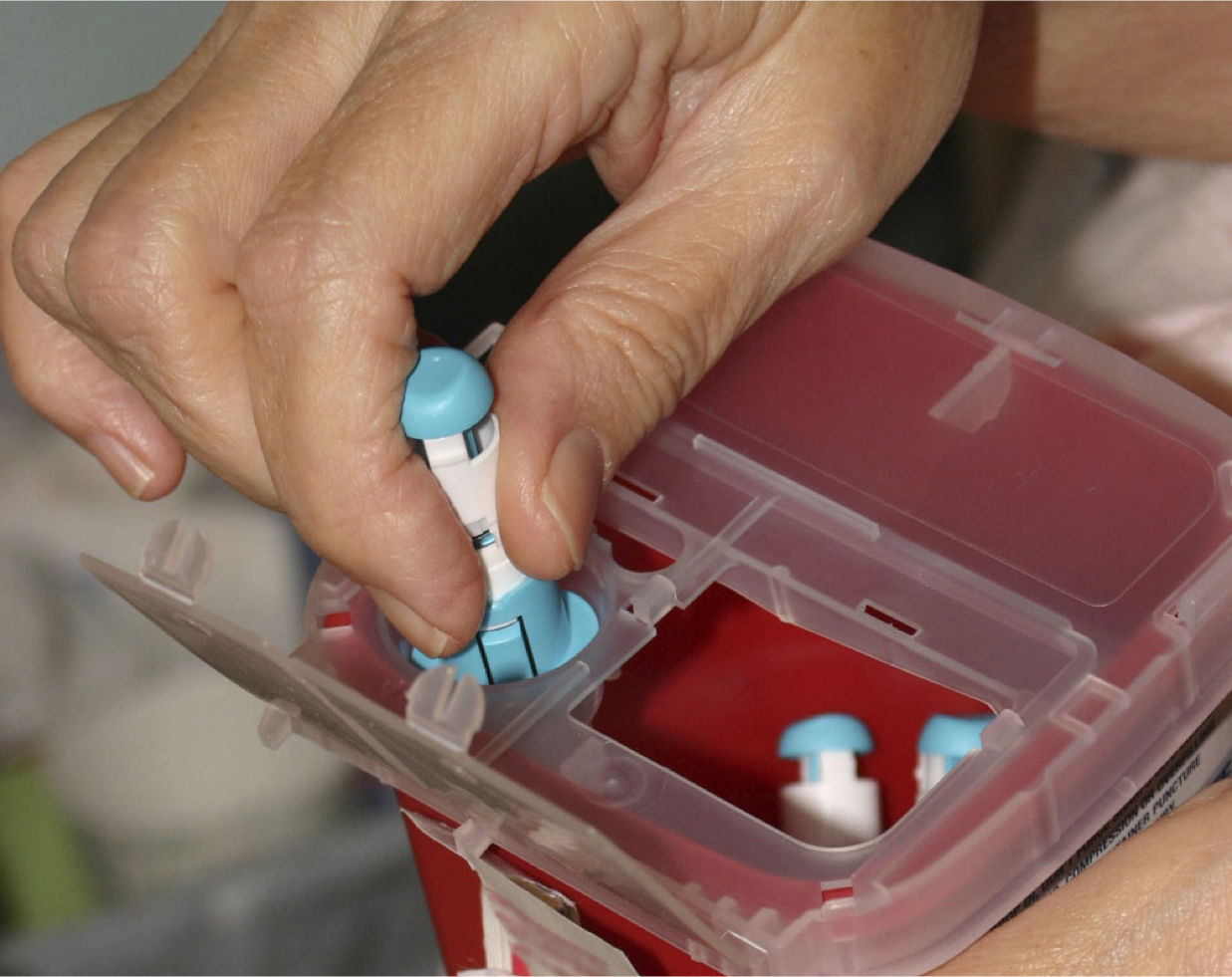 A hand putting a used needle into a sharps container.