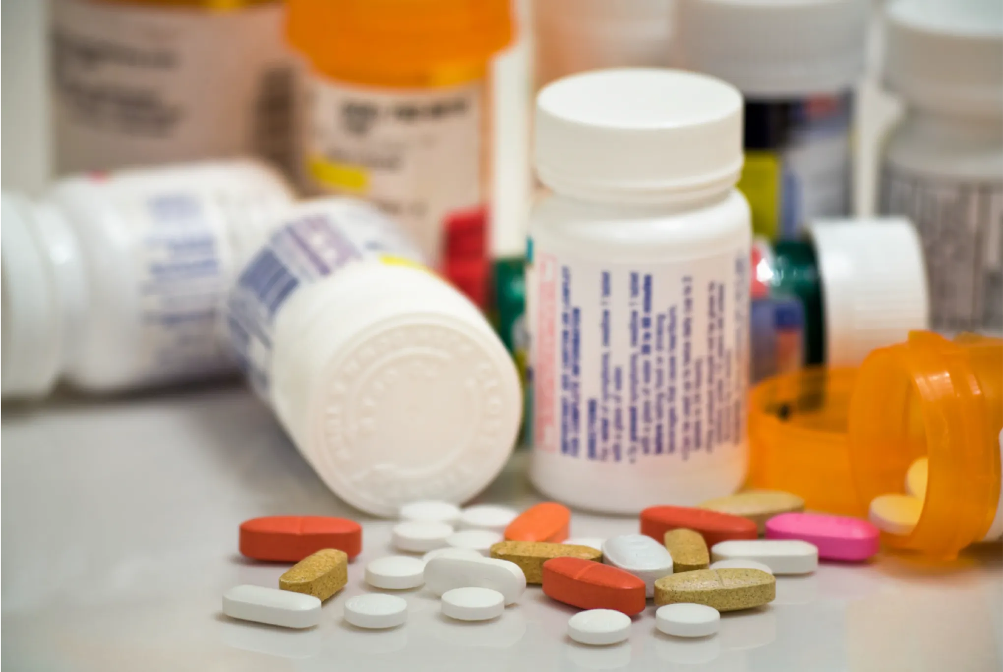 A few pill bottles on a table with some spilled out in various colors.